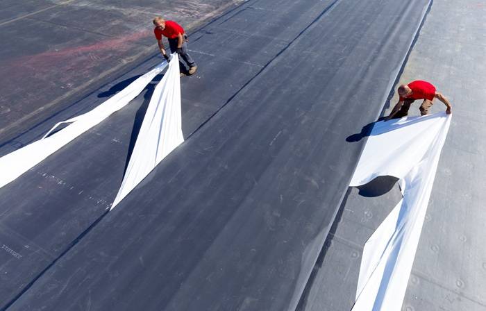 Due operai in maglia rossa lavorano all'impermeabilizzazione della copertura con l'utilizzo di una membrana EPDM