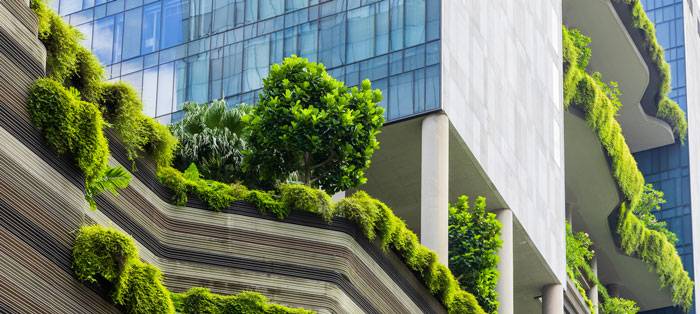 Facciata di edificio commerciale con verde verticale e terrazze vegetate per sostenibilità ambientale ed efficienza energetica.