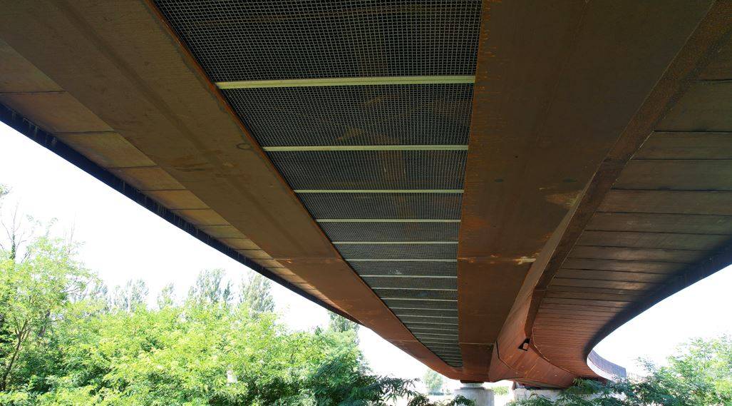 Vista dell’intradosso del ponte sul Tevere a Sansepolcro con cassone curvo in acciaio Corten, grigliato di chiusura inferiore e geometria tridimensionale dell’impalcato misto