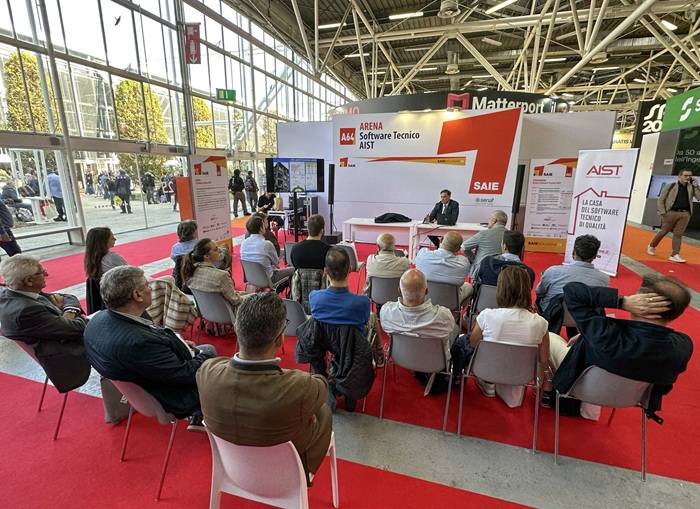 Un gruppo di professionisti partecipa a un convegno nell’Arena Software Tecnico AIST durante il SAIE, il Salone Internazionale dell’Edilizia, in uno spazio espositivo luminoso con allestimento rosso e bianco.