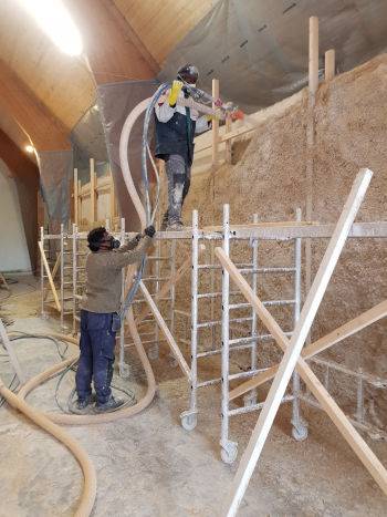 Costruire in canapa e calce, operai al lavoro con macchina spruzzatrice