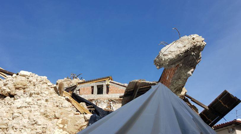 Resti di cordolo in cemento armato tra le macerie di un edificio crollato dopo il sisma: barre d’armatura visibili e muratura disgregata.