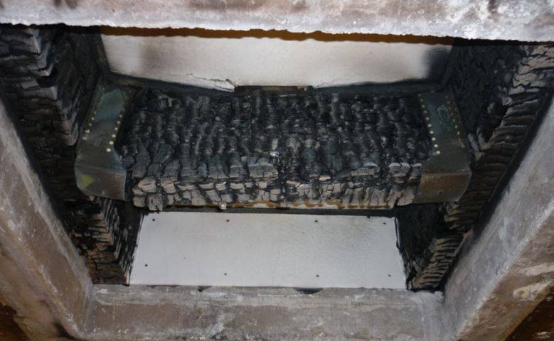 Dettaglio dei danni strutturali post-incendio su un elemento costruttivo in legno. Si notano la perdita di massa e l'alterazione della struttura lignea a causa delle alte temperature.