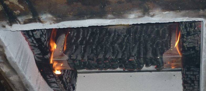 Fase avanzata di una prova di resistenza al fuoco su un componente edilizio in legno. Si osservano chiaramente gli effetti della carbonizzazione e l'azione diretta delle fiamme.