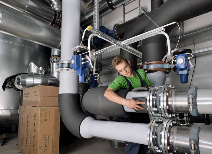 Tecnico installa isolamento elastomerico a celle chiuse su tubazioni HVAC per efficienza energetica e controllo condensa in edificio commerciale.