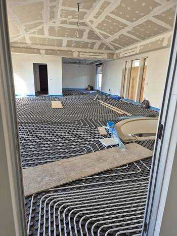 Interno di un edificio in fase di ristrutturazione con impianto di riscaldamento a pavimento installato su tutta la superficie. Si vedono le serpentine dei tubi posate sul sottofondo, mentre il soffitto in cartongesso e le pareti sono ancora in lavorazione
