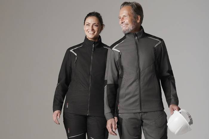 Due persone, un uomo e una donna, indossano abbigliamento da lavoro coordinato di colore nero e grigio con dettagli riflettenti. Entrambi sorridono e camminano fianco a fianco, con l’uomo che tiene in mano un casco protettivo bianco. Lo sfondo è neutro e chiaro.