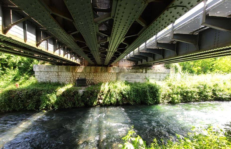 Vista inferiore delle travate metalliche ammalorate del ponte ferroviario Roma-Cassino sopra il corso d'acqua vincolato.