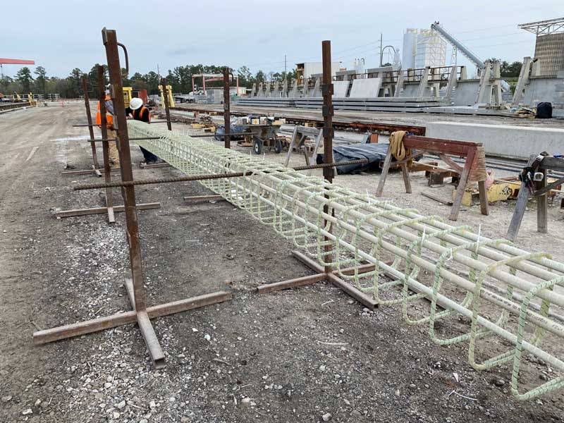 Operai assemblano la gabbia di armatura longitudinale e staffe in barre GFRP per una trave prefabbricata leggera e priva di metallo.