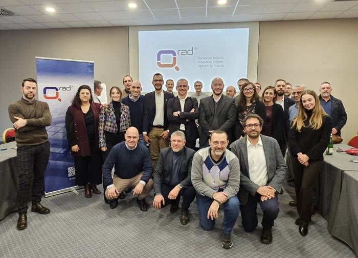 Gruppo dei rappresentanti delle aziende del Consorzio Q-RAD riuniti durante un incontro ufficiale, posano per una foto davanti allo schermo con il logo del Consorzio Italiano Produttori Sistemi Radianti di Qualità.